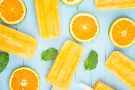 Homemade frosty ice cream stick with oranges on a blue wooden backgroundの写真素材