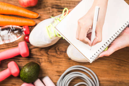 Healthy concept with nutrition food in lunch box and fitness equipment with woman writing time to...