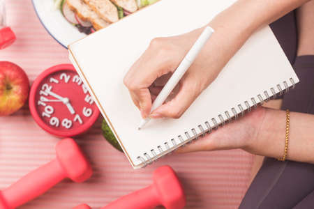 Healthy concept with nutrition food in lunch box and fitness equipments with woman writing time to...