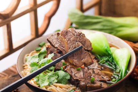 Spicy red soup beef noodle in a bowl on wooden tableの写真素材