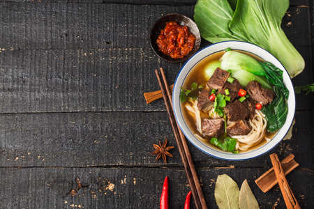Spicy red soup beef noodle in a bowl on wooden tableの写真素材