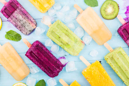 Various fruit ice cream on stick are placed on the blue wooden board backgroundの写真素材