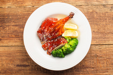 Roast duck with broccoli and lemon in white plate on wooden backgroundの写真素材