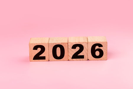 Wooden cubes form the word 2026 on a pink background.