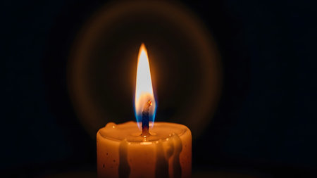 A lit white candle glows with a bright flame and a soft, circular light effect in darkness.の写真素材