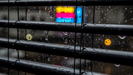 Stock showing rainy window with blinds and reflected neon lights in water droplets.