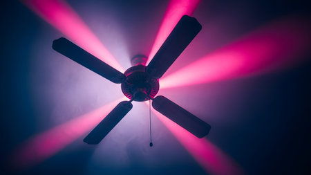 A dark interior space a ceiling fan with intense pink light beams radiating outwards and wisps...の写真素材