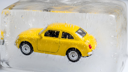 A vibrant yellow toy car is completely encased in a clear block of ice, showcasing air bubbles...の写真素材