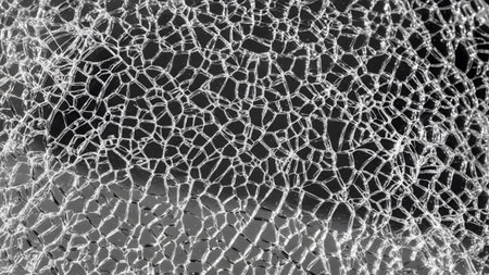 A close-up texture of cracked glass showing a dense network of fine fracture lines against a...