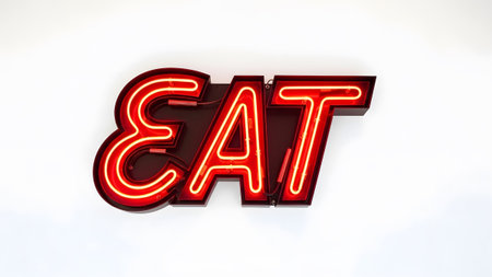 Sign showing bright red neon eat sign mounted on a dark surface against a white backdrop.の写真素材