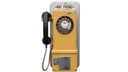 A vintage yellow payphone with a black handset and rotary dial stands isolated on a white...の写真素材