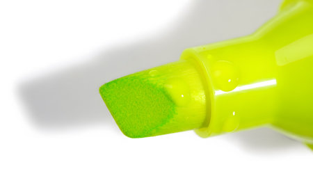 A vivid green highlighter pen tip is shown up close, with several clear water droplets resting...