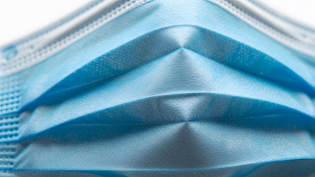 showing close-up macro shot of a blue disposable medical face mask with pleated folds....