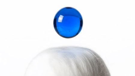 Above showing blue glass marble levitating above fluffy white fibers on a white background.