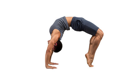 Athletic man in grey t-shirt and dark shorts executes a challenging back bridge pose, isolated...