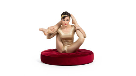A flexible contortionist in a gold leotard sits on a red cushion, demonstrating an intricate...の写真素材