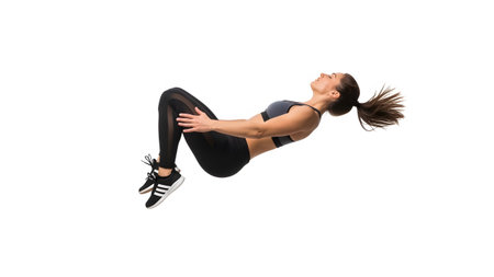 A woman in black athletic wear is captured mid-air performing a backward flip with knees tucked...