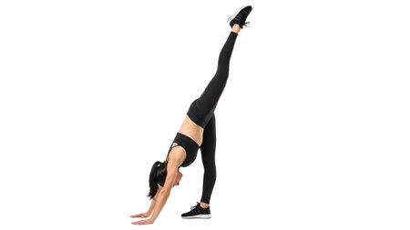 A woman in black athletic wear performs a handstand with one leg extended upwards on a white...