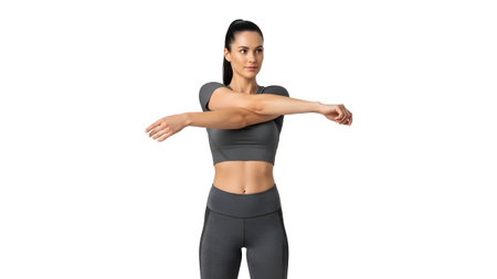 A woman with dark hair in a ponytail stands with arms crossed over her chest, stretching her...