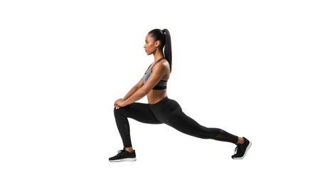 A woman in black leggings and a sports bra stretches in a lunge pose, her body isolated on a...