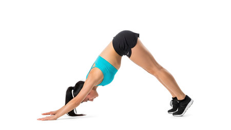 A woman in athletic wear holds a downward dog pose with arms and legs extended on a white...