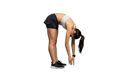 A woman in a white sports bra and black shorts bends forward with her arms reaching towards the...