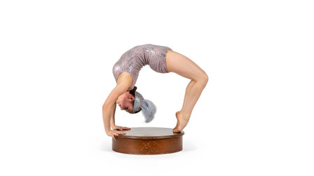A woman in a sparkly leotard and feather headpiece holds a backbend pose on a wooden platform.