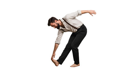 A man with a beard and suspenders stretches his leg forward, touching his toes with his hand.