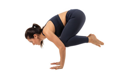 A woman in dark blue activewear balances in the Crow Pose on a white background, focused and strong.の写真素材