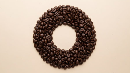 A circular arrangement of dark roasted coffee beans centered on a plain light beige background.