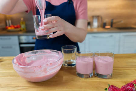 the process of making a strawberry dessert from milk. Cook puts the pudding in cups and decorates with berriesの写真素材