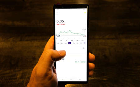 Male hand holding smartphone with mobile app. Trader analyzing stock trading graph. close upの写真素材