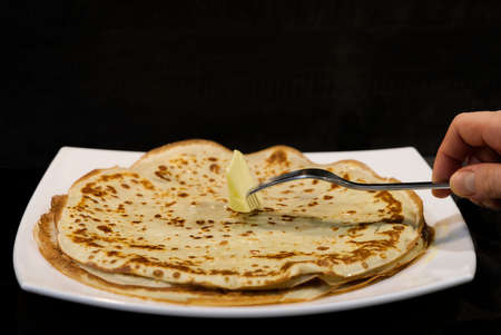 Golden pancakes with butter on a white plate. Isolated black background. close up