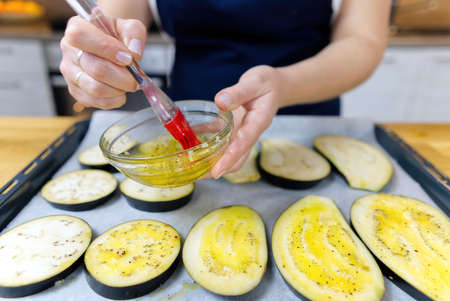 brushing with oil sliced eggplant on a baking tray. grilled eggplant appetizer cooking process. close upの写真素材