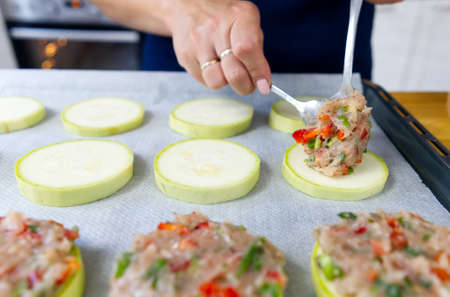 Zucchini stuffed with raw minced meat and vegetables on a baking sheet. female hands spread the...