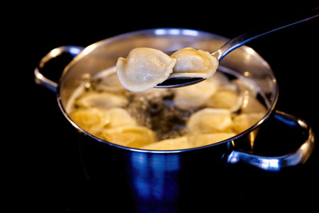 Dumplings mixed with a spoon in a pot of boiling water. Boiled dumplings in a pan. black background close upの写真素材