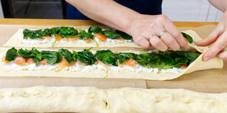 the cook puts spinach and trout on the dough. Savory Christmas pie in the shape of a wreath cooking process. close upの写真素材