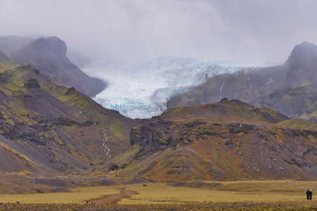 Two persons are looking towards the highlands and the glacier and the moss covered mountains in Icelandの写真素材