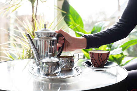 womans hand holding hot teapot in morning sunlight, retro colors, a window through which the sun...