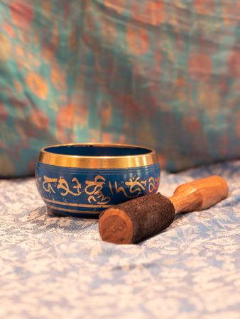 Haulerwijk - march 07 2020: Haulerwijk, The Netherlands. Blue and golden singing bowl made of seven metals with a wooden striker on an Indian scarfのeditorial素材