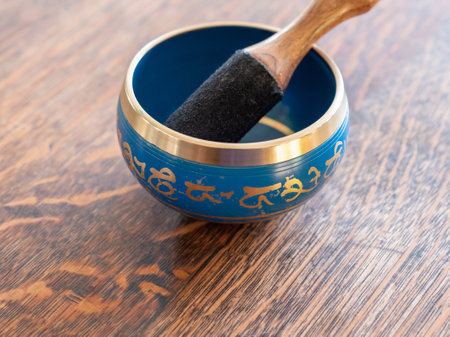 Haulerwijk - march 07 2020: Haulerwijk, The Netherlands. blue and golden indian singing bowl made of seven metals with a wooden striker on a wooden tableのeditorial素材