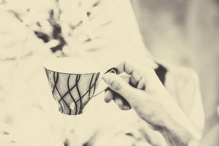 vintage tee cup on green flower background, the sun shines through the window, woman hand.の写真素材