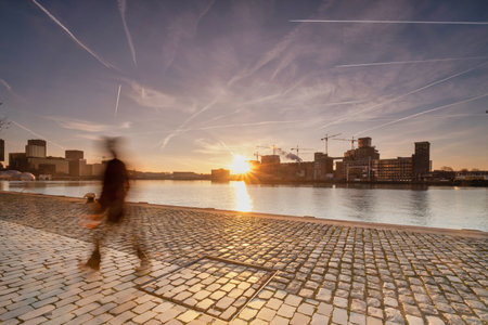 Rotterdam - 14 February 2019: Rotterdam, The Netherlands The sun rises behind several old industrial buildings on the waterfront early in the morning, Extinct city street only one person completely out of focus in foreground. South Holland, Rotterdam, Netのeditorial素材