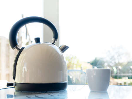 Electric kettle with boiling water for the herbal tea on a tble in front of a window. Selective...