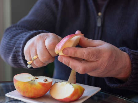 Old man hands peeling organic red Pink Lady apple outside over a bowl of apple slices
