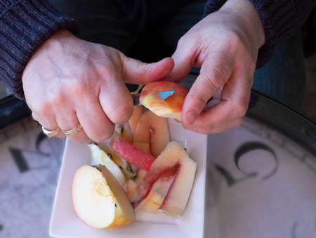 Old man hands peeling organic red Pink Lady apple outside over a bowl of apple slices.