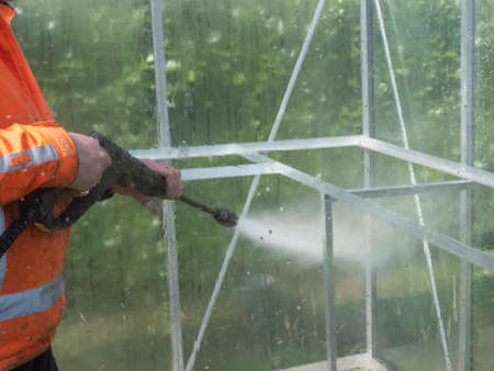 Construction worker cleaning filth with high pressure cleaner from a glass greenhouse