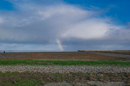 Rainbow  dark blue sky  clouds. grass and stones in foreground. People in the distance. The...