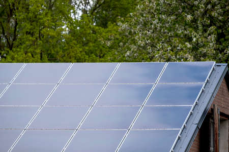Roof with solar panel reflecting the clouds, on the roof of a farm, trees in background