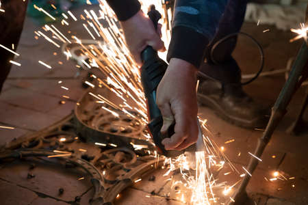 Front view of a man's hands working on a metal part of a garden bench, using an electric grinder...